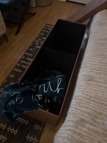 Wooden storage bench with an open lid, revealing a blanket inside. The bench is located next to a striped couch