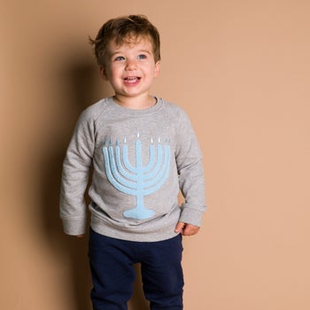 a child in a grey sweatshirt with a light blue menorah embroidered on it