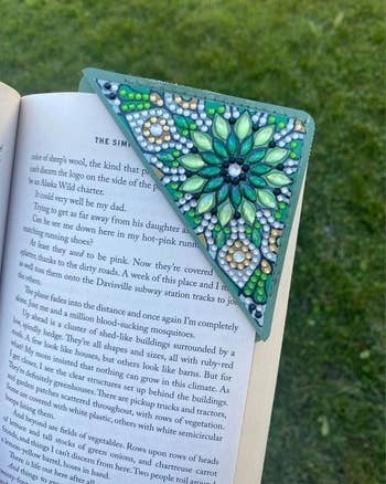 Decorative, beaded corner bookmark holds a page in an open book, placed on grass