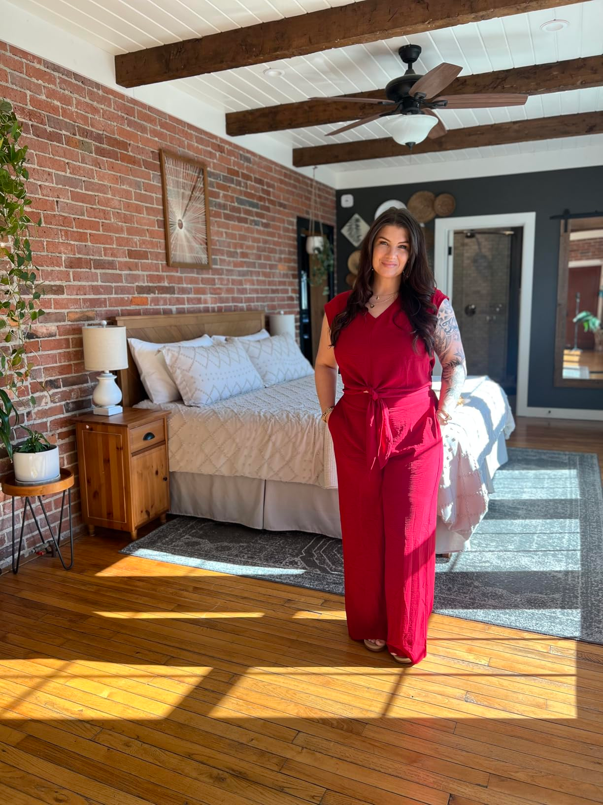 Person successful  a stylish, sleeveless jumpsuit stands successful  a modern   chamber  with exposed ceramic  walls and woody  beams, suggesting location  decor shopping