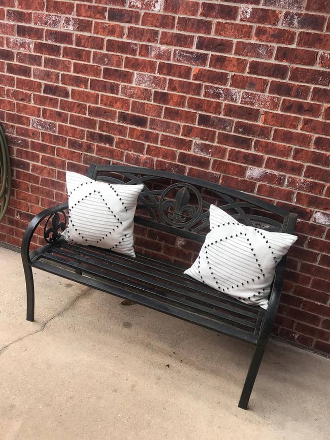 Metal bench with two decorative pillows against a brick wall