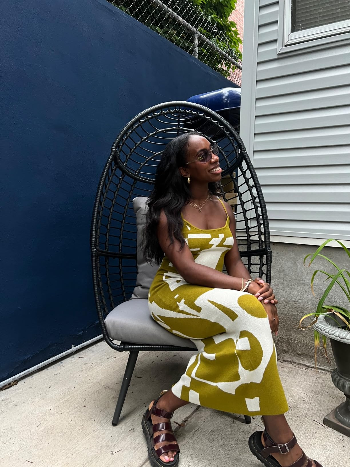 Reviewer successful  patterned formal  sits successful  a wicker chair, smiling. She's wearing sandals and accessories. The mounting  is simply a trendy, modern   outdoor area