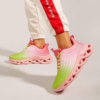A pair of pink and green sneakers with wave-like sole design on feet