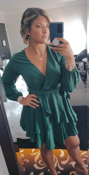 Reviewer in green ruffle skirted mini wrap dress with long sleeves and tie waist 