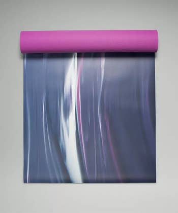the mineral blue and vivid plum-colored yoga mat being unrolled, showing how the bottom is a different color