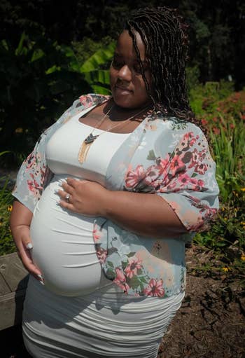 Pregnant pistillate successful a fitted formal and floral shawl stands outdoors, mildly holding her belly