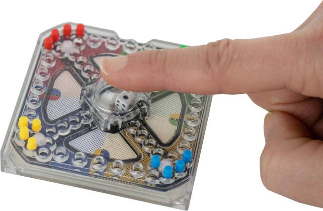 Finger pressing pop-o-matic dice connected  a committee  game, with colorful crippled  pieces visible. Suitable for household  gaming and amusement  buying  articles