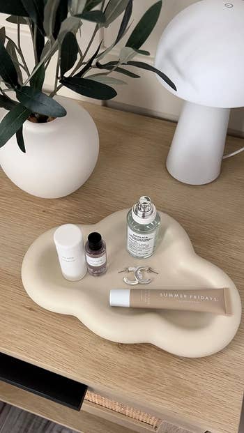 reviewer's cloud tray with  jewelry, lipgloss, and perfumes on it