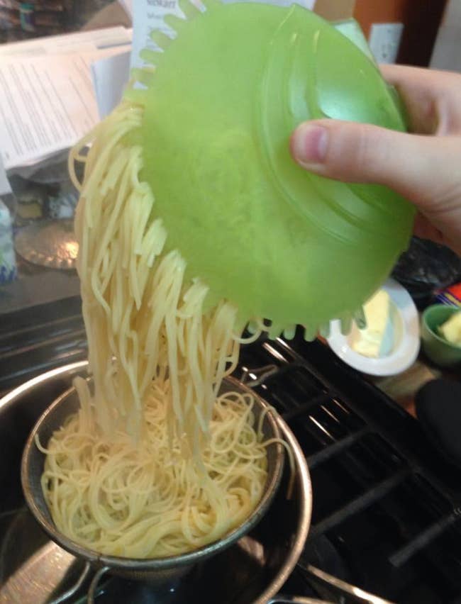 Reviewer using a green hand-sized silicone gripper to pull a serving of noodles out of a pot 