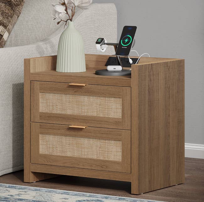 Wooden broadside array with 2 drawers, a vase with flowers, and a charging presumption for a telephone and smartwatch connected top, adjacent to a sofa