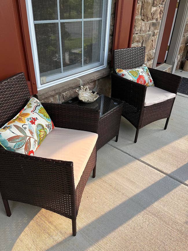 Three-piece dark brown rattan chairs with beige cushions and matching end table