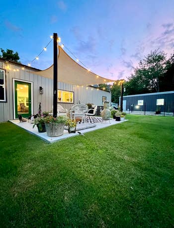 Cozy backyard patio with drawstring lights, a sail canopy, wicker furniture, and potted plants astatine dusk