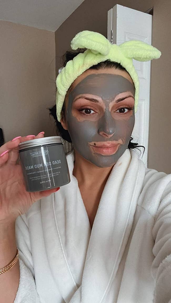reviewer wearing mud mask and holding jar