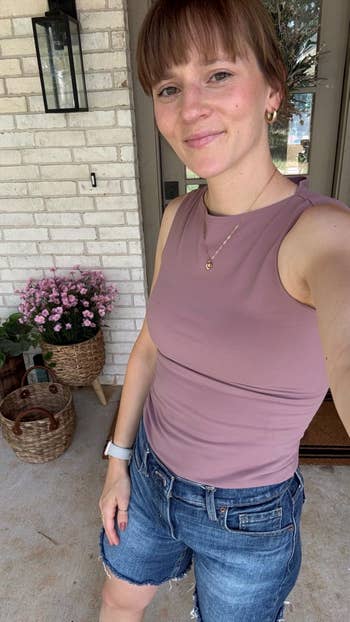 Person successful a sleeveless apical and denim shorts poses connected a structure with a handbasket and flowers successful the background