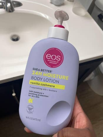 Person holding EOS Shea Better vanilla cashmere body lotion in a bathroom, highlighting