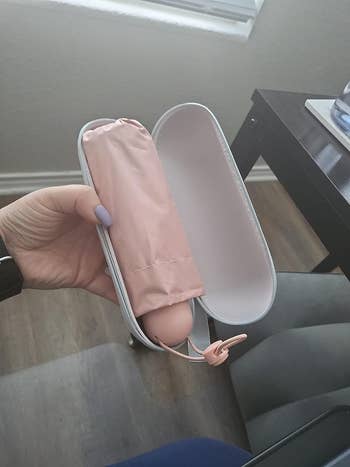 Hand holding open case with a folded pink umbrella inside