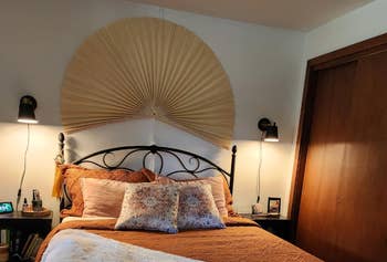 Bedroom with a large wall fan decor above an ornate headboard, flanked by lit wall lamps
