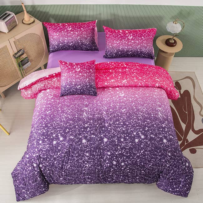 Pink and purple glitter ombre patterned comforter with purple sheets and matching glitter pillow cases against a green wall
