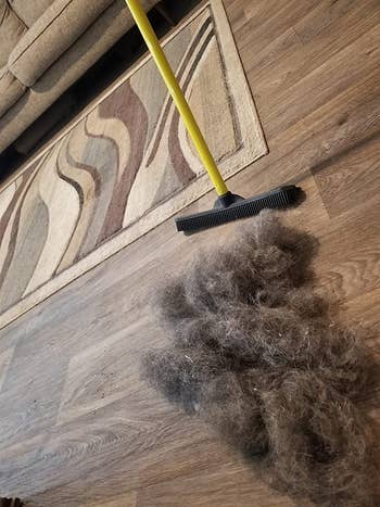 same broom next to gigantic pile of gray dog fur on hardwood floor