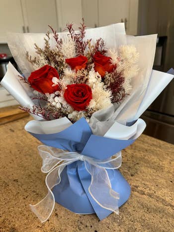 reviewer's bouquet of red roses mixed with white and brown dried flowers, wrapped in blue paper with a sheer ribbon, placed on a kitchen counter