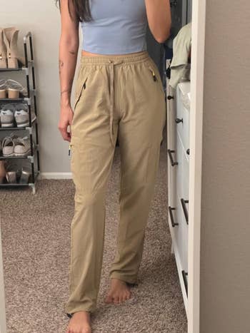 Person in beige cargo pants and a light tank top stands barefoot in a bedroom with a shoe rack and dresser