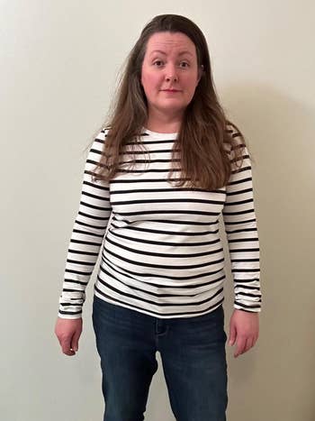 Person lasting against a plain background, wearing a striped long-sleeve garment and jeans with hands by their sides