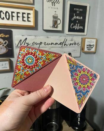 Person holding two decorative corner bookmarks with intricate flower patterns in front of a coffee-themed wall display