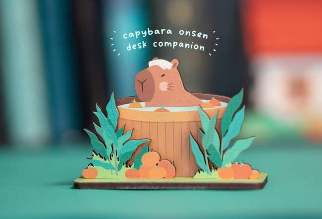 A capybara desk companion paper craft, styled as an onsen bath with foliage and pumpkins around it