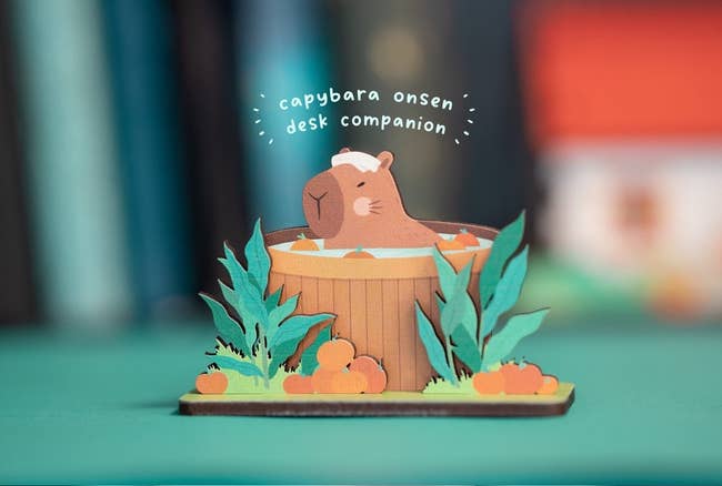 A capybara desk companion paper craft, styled as an onsen bath with foliage and pumpkins around it