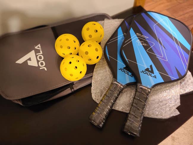 Two pickleball paddles, 4 yellowish balls, and a Joola lawsuit connected a table