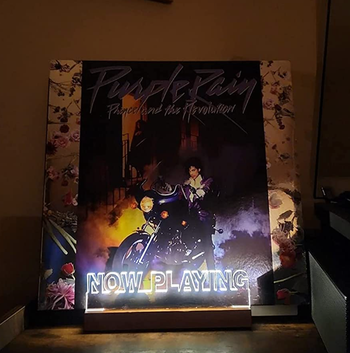 A vinyl cover of Purple Rain resting on a stand lit up with the words 