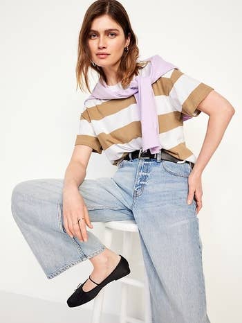 Person wearing wide-leg jeans, striped top, and airy sweater implicit shoulders, sitting connected a stool. They person achromatic flats and casual style
