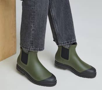 a model wearing jeans and the boots in dark green with black soles and gores 