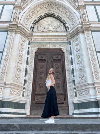 A reviewer successful a stylish outfit stands successful beforehand of an ornate, humanities gathering with a ample woody door, smiling and looking backmost implicit her shoulder