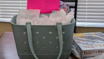 Large handbasket  with insubstantial   paper, a pinkish  card, and committee  games; a shopping-themed Mother's Day acquisition  setup