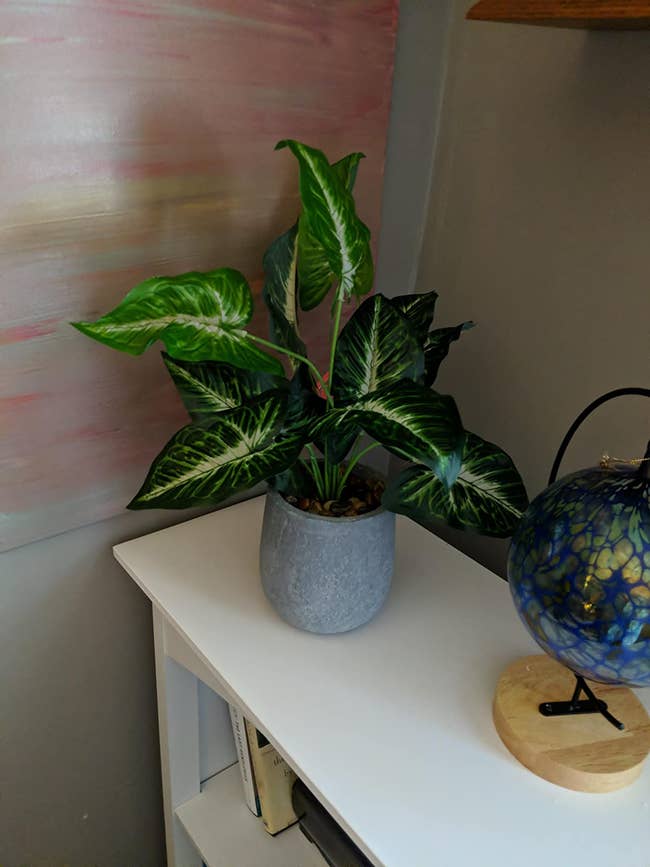 faux plant with large leaves in a gray pot on top of a bookshelf