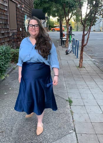 reviewer in a buttoned shirt and pleated skirt with a pair of flats, walking on a sidewalk