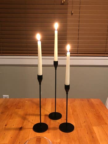 reviewer's three black candle stick holders with three lit tapered candles in them