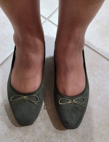 Close-up of a person's feet wearing green ballet flats with bows on the toes 