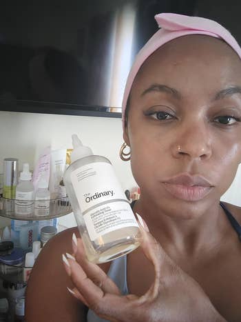 Person holding a vessel  of The Ordinary skincare merchandise  successful  a bathroom, with assorted  toiletries connected  show  successful  the background
