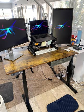 reviewer's desk setup with three screens on the electric standing desk