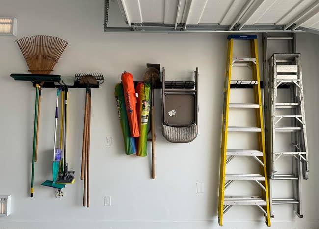 Wall-mounted retention strategy holding plot tools similar rakes, a ladder, and a folding chair