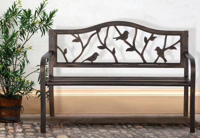 Metal bench with bird design next to a plant