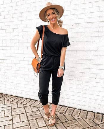 Model wearing the black jumpsuit with a wide-brimmed hat, sandals, and crossbody bag