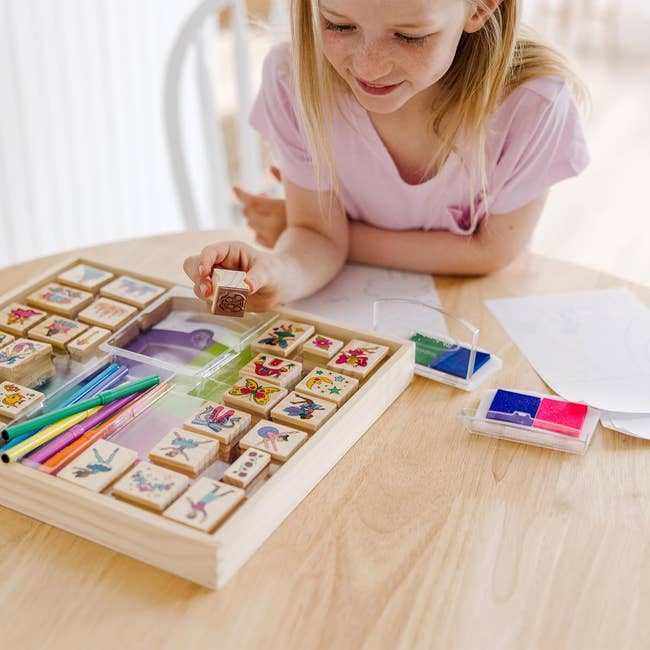 Child playing with a woody stamp acceptable connected a table, surrounded by colorful pencils and paper, suggesting a originative activity