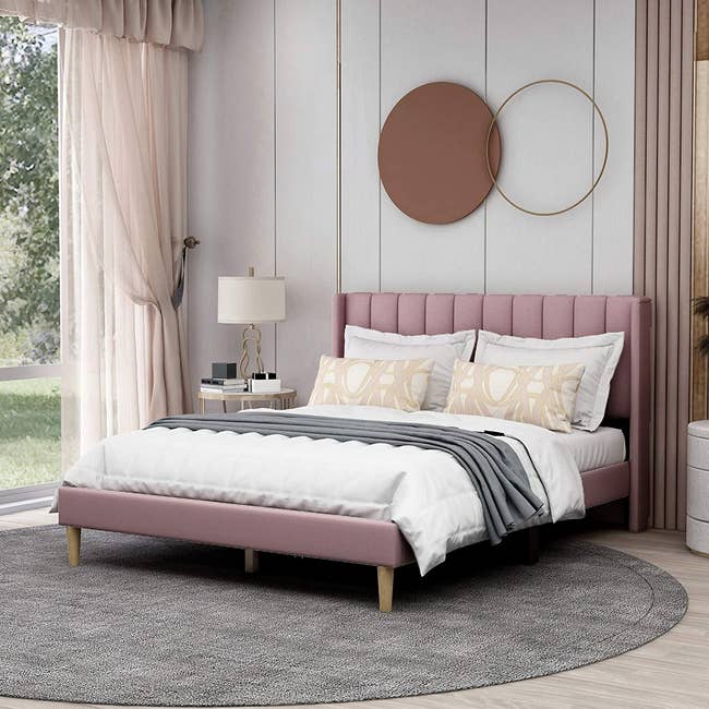 the pink upholstered bed frame with four blonde wooden legs