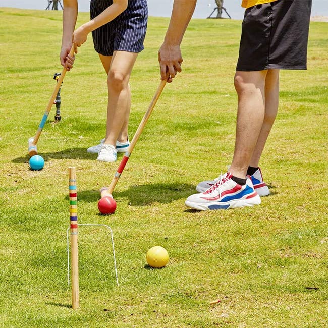 Two radical playing croquet connected grass, each with a woody mallet