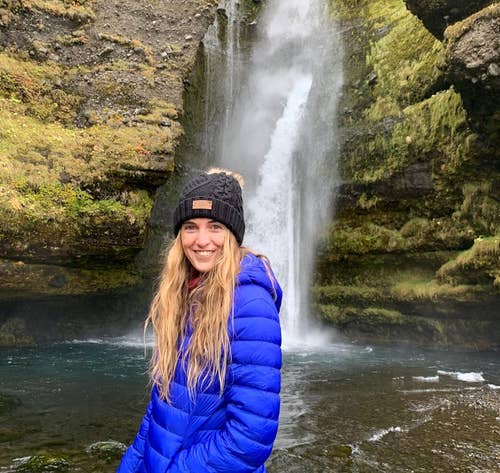A reviewer wearing the blue puffer jacket in fron of a waterfall in Iceland