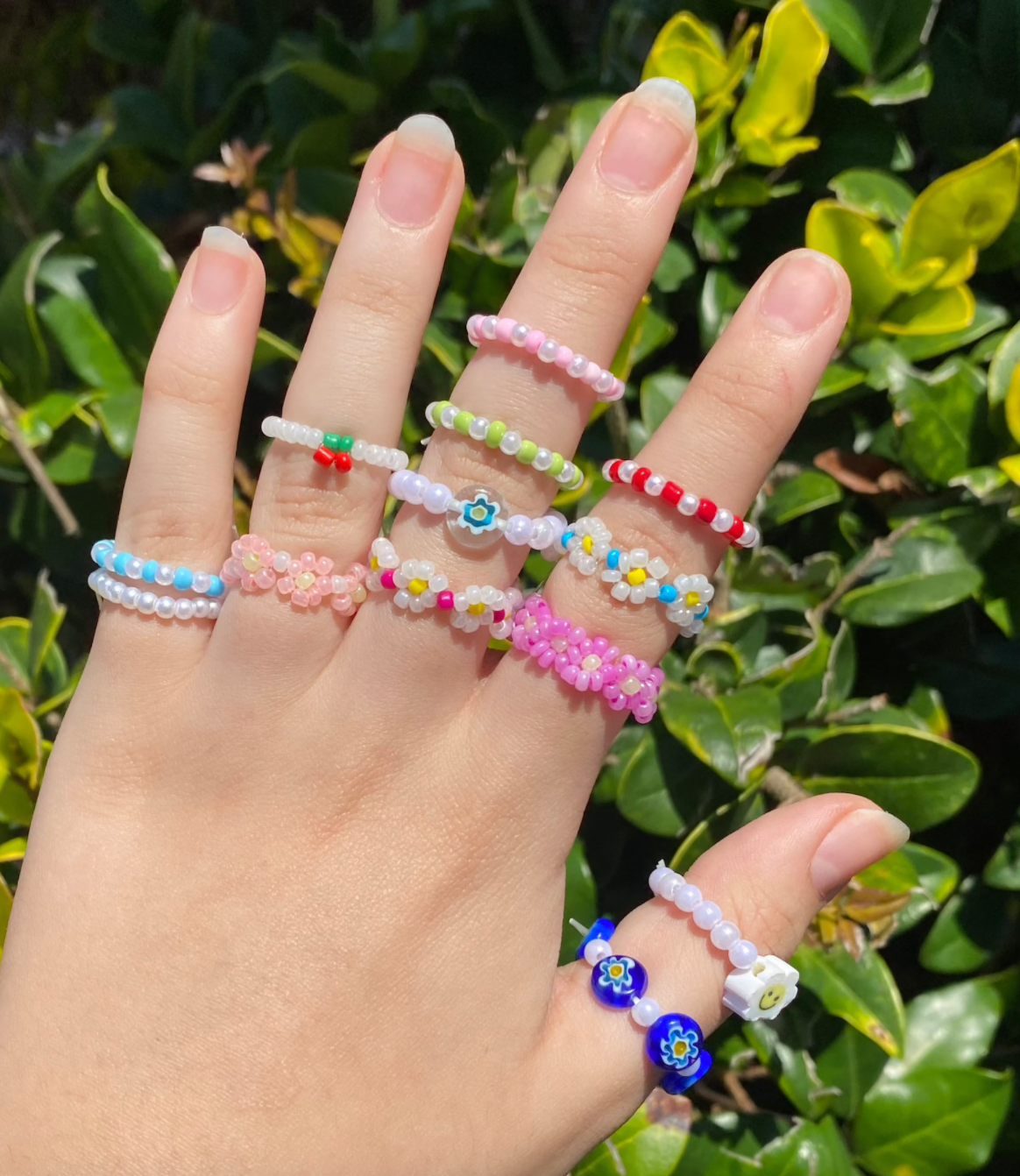 hand with a variety of colorful seed bead rings on all five fingers