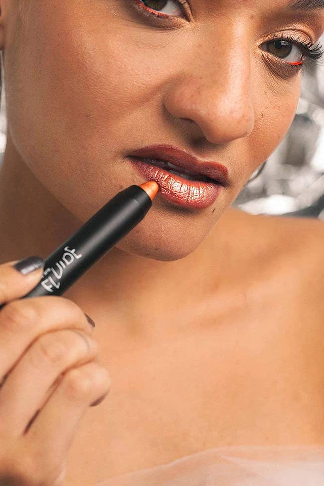 Model applying coppery orange colored crayon to lip 